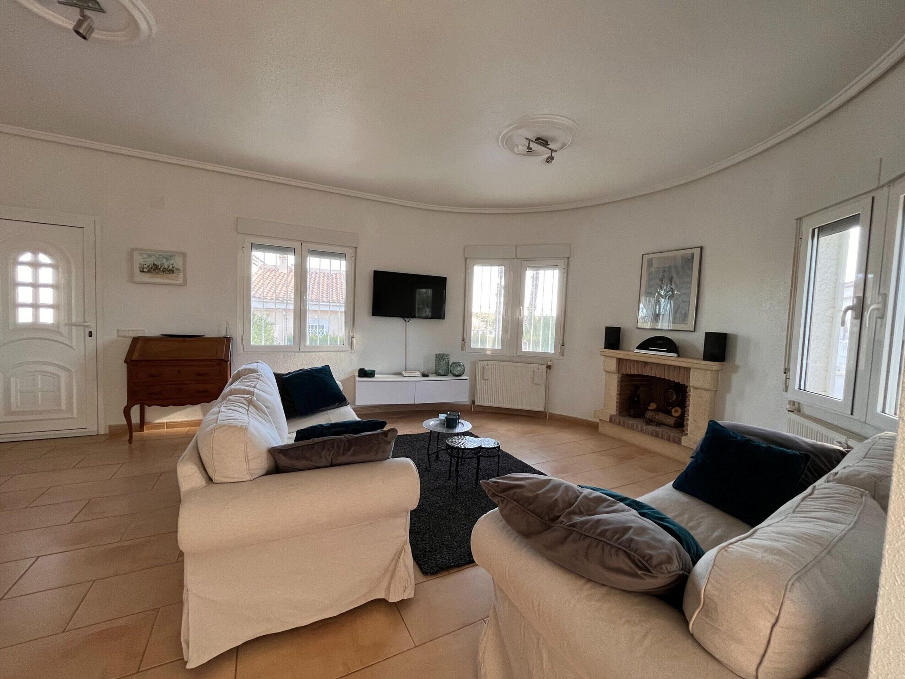 A living room with a sofa set, a television, a fireplace, and a window.