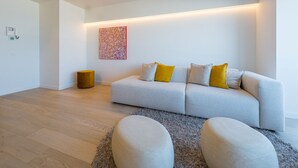 A modern living room with a grey sofa, two yellow cushions, a round gold side table, and a colorful abstract painting on the wall. - Beautiful Apartment With Direct sea View (Middelkerke)