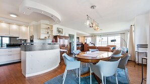 Una cuina moderna amb armaris blancs, una illa central i una zona de dinar amb una taula rodona i seients.