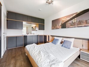 A modern bedroom with a large bed, built-in wardrobe, and a cityscape view. - Castle Apartment With View (Blankenberge)