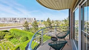 Un balcó amb dues cadires, una taula i vista sobre un paisatge urbà ple d'edificis i vegetació.