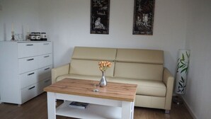 Ein Wohnzimmer mit einem beigefarbenen Sofa, einem Holztisch, einer weißen Kommode und zwei gerahmten Kunstwerken an der Wand.