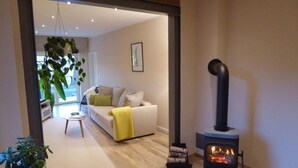 A living room with a sofa, a yellow throw blanket, a black wood stove, and a potted plant.