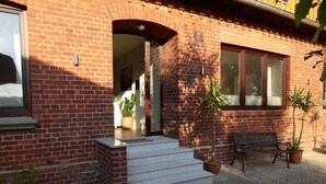A brick building with a front entrance, steps, a bench, and potted plants.