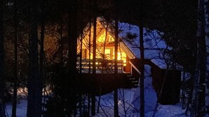 Una baita con un patio in legno e un'ampia finestra, circondata da alberi e neve.