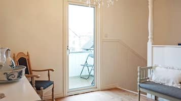 A room with a wooden floor, a white bench, a chair, a table with a pitcher, and a chandelier.