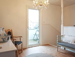 A room with a wooden floor, a white bench, a chair, a table with a pitcher, and a chandelier. - 4 Star Holiday Home in Lysekil (Lysekil)
