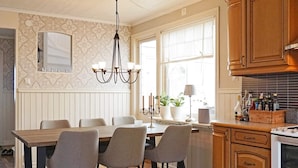 A kitchen with a dining table, chairs, a chandelier, a window with curtains, and wooden cabinets. - 4 Star Holiday Home in Lysekil (Lysekil)