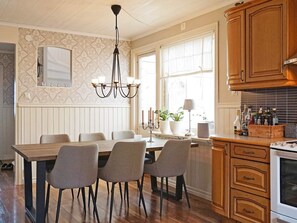 A kitchen with a dining table, chairs, a chandelier, a window with curtains, and wooden cabinets. - 4 Star Holiday Home in Lysekil (Lysekil)