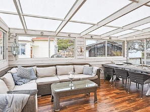 A sunroom with a glass ceiling, a sofa, a coffee table, and a dining area with chairs. - 4 Star Holiday Home in Lysekil (Lysekil)