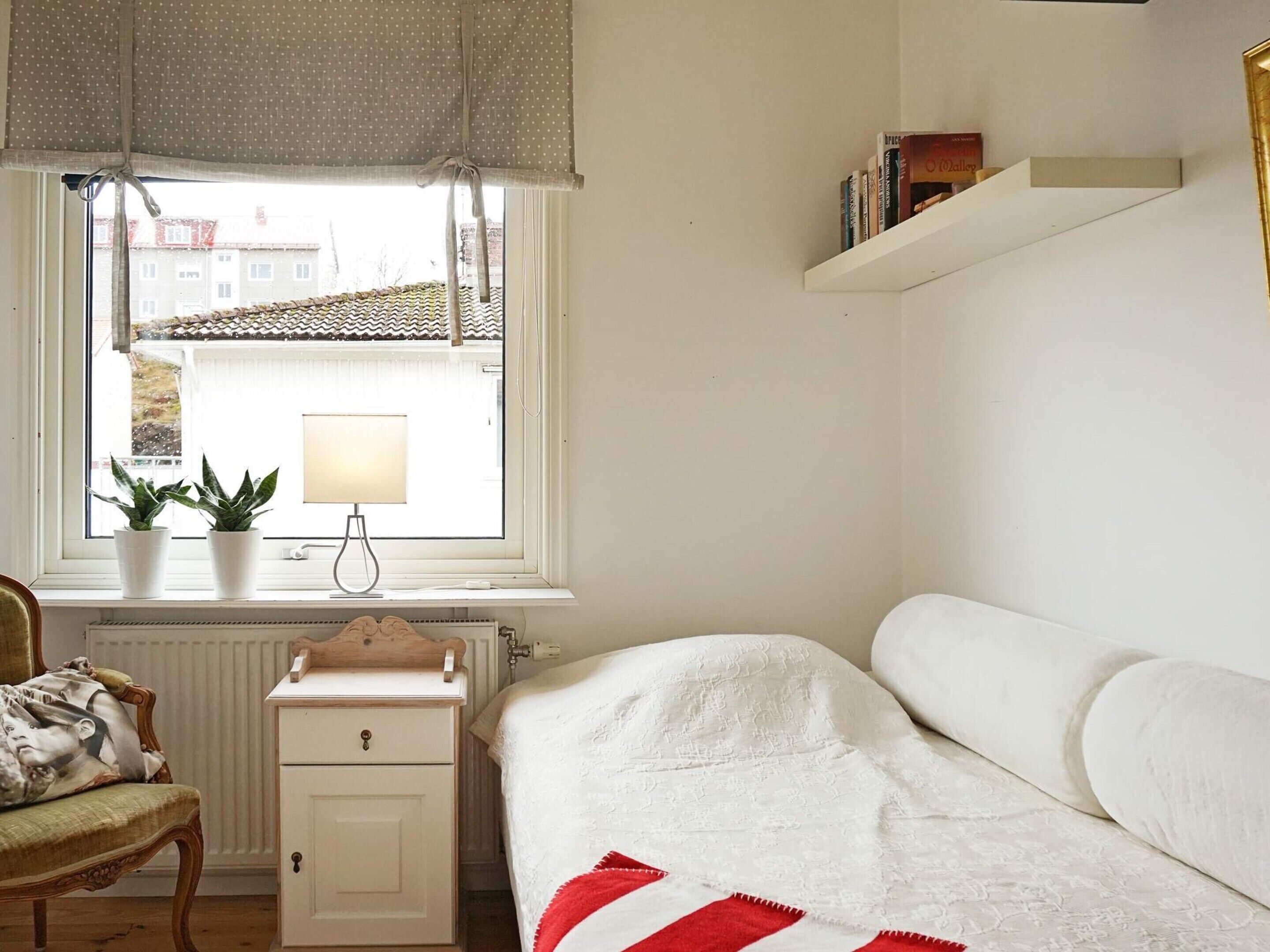 A bedroom with a bed, a bedside table, a lamp, a chair, and a window with a view of buildings.