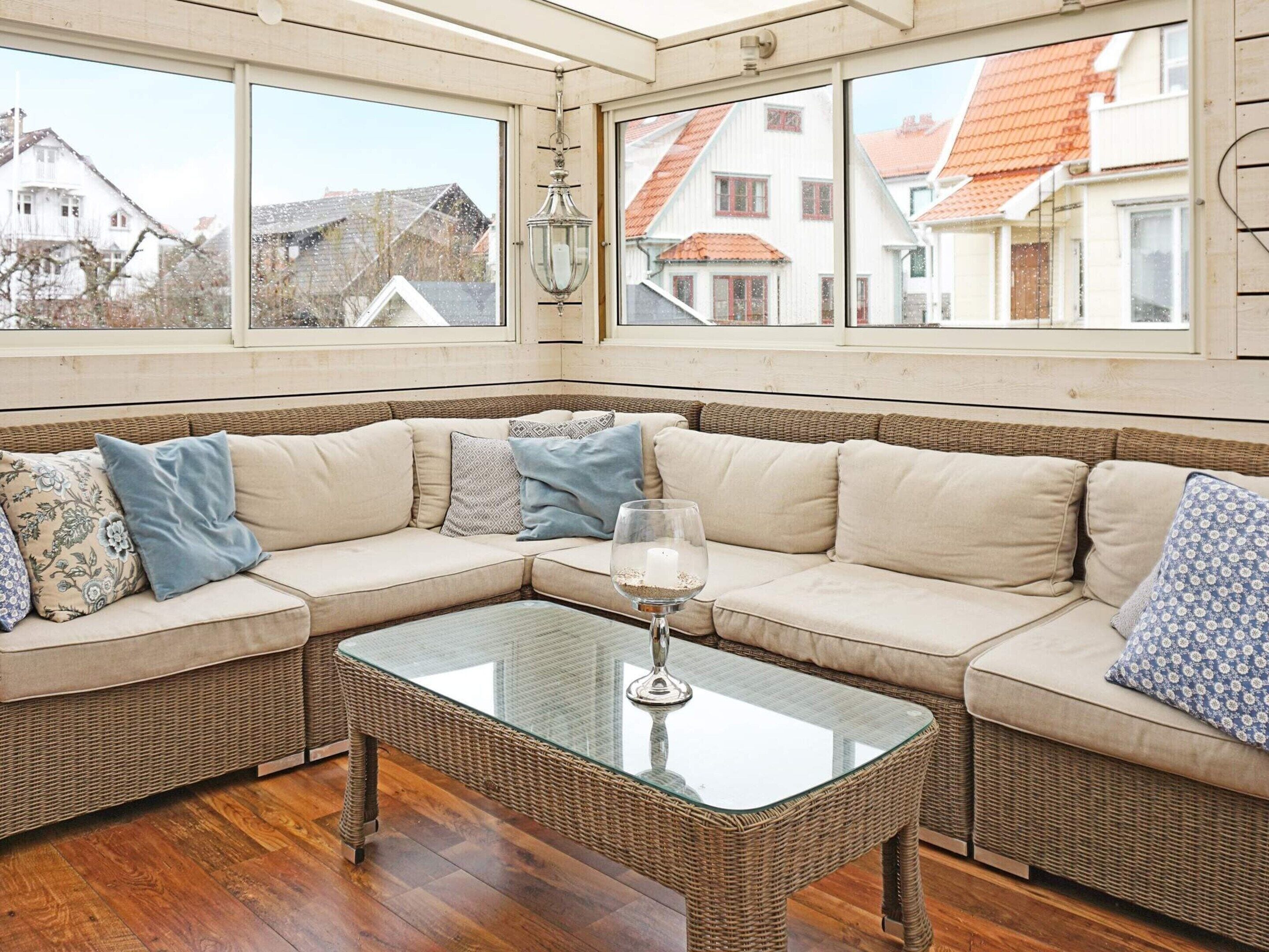 A corner seating area with a glass-top table, wicker furniture, and a view of neighboring houses through large windows.