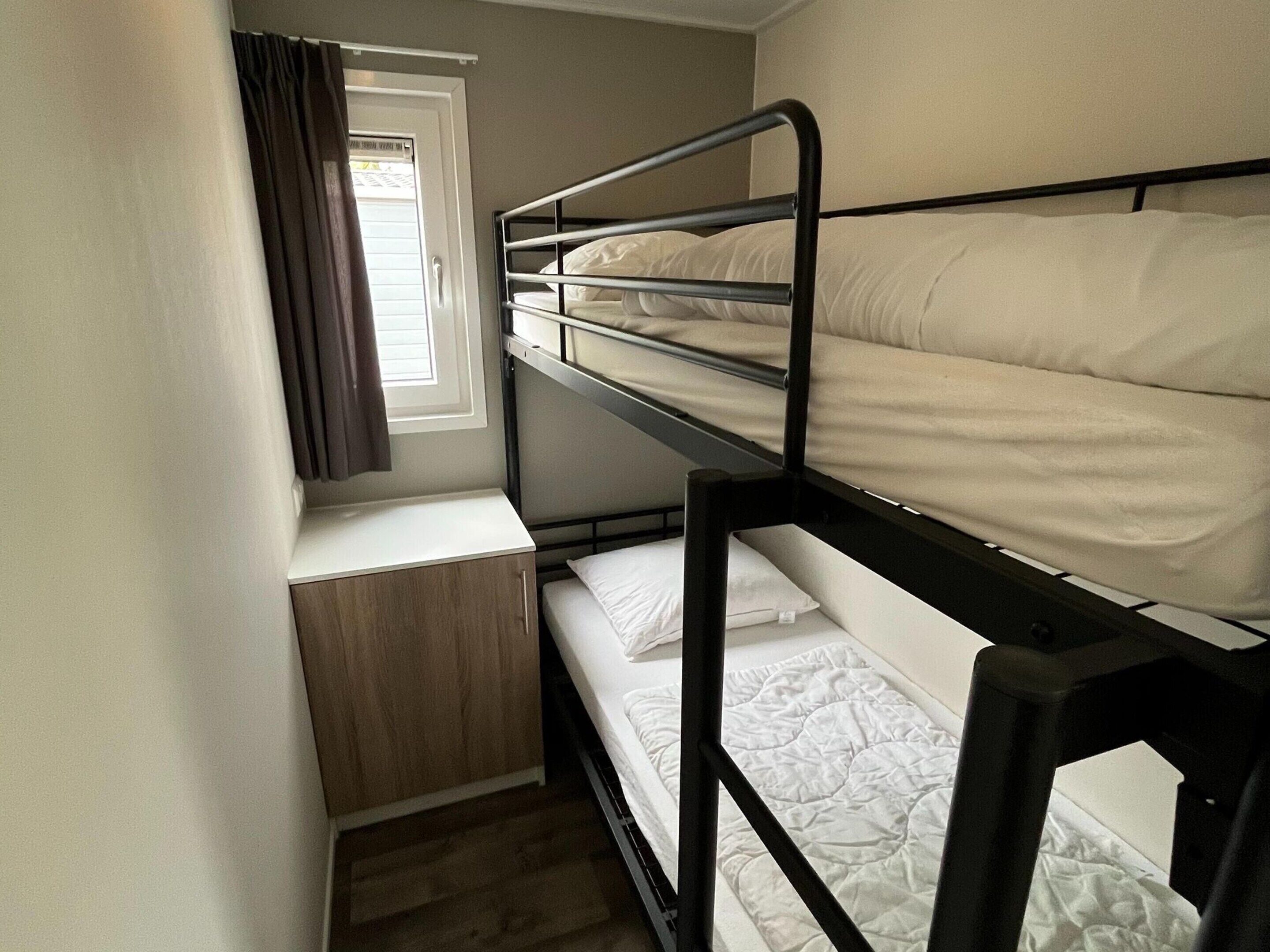 A bunk bed room with a window and a small wooden cabinet.