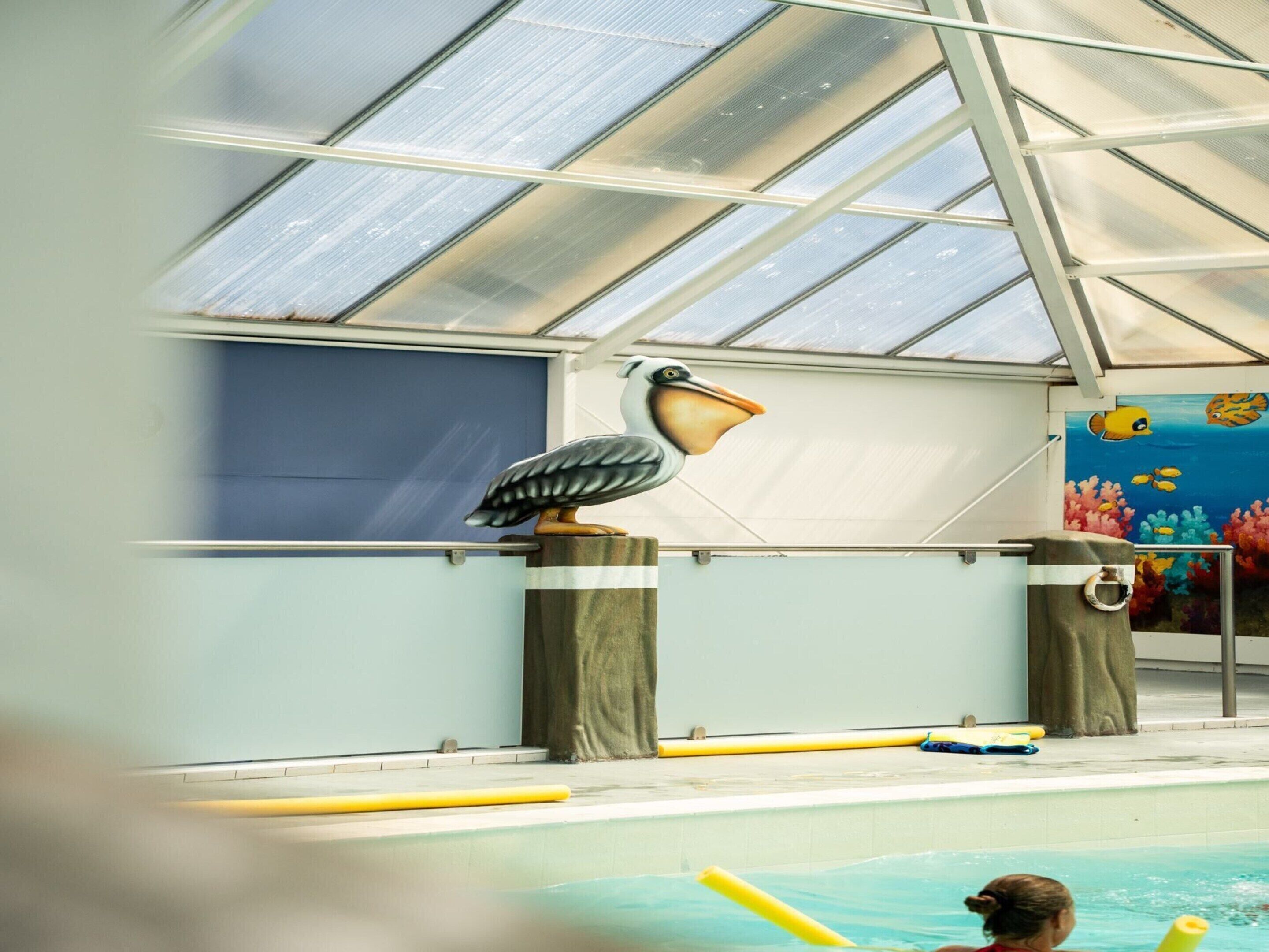 Une piscine intérieure agrémentée d’une grande sculpture d’oiseau, d’une fresque représentant des poissons et d’un plafond en verre.
