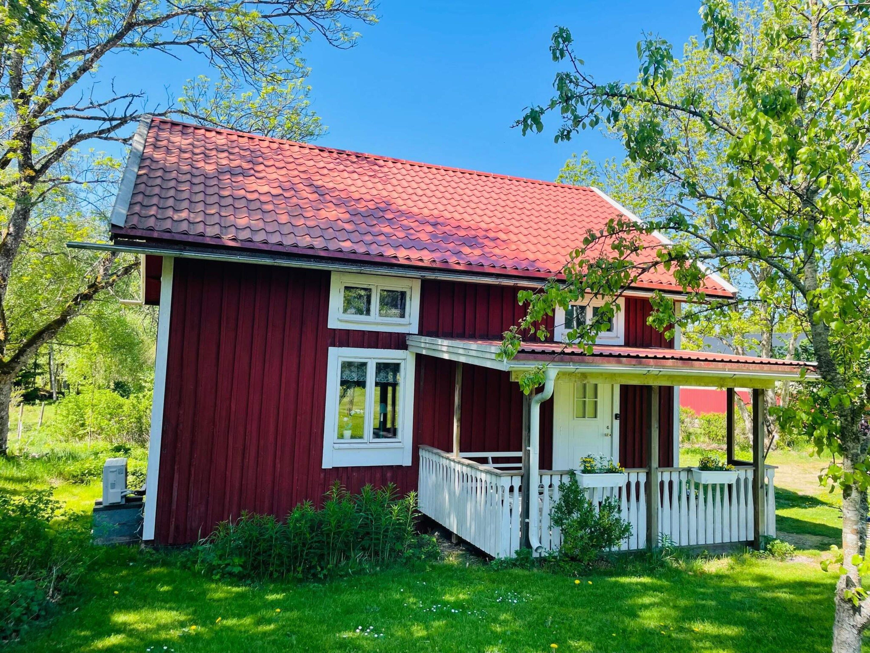 Ett rött trähus med en vit veranda och en liten trädgård.