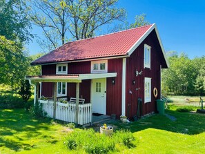 A red wooden house with a white porch, a small garden, and a pond.