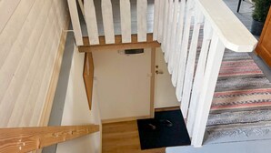 A staircase with a wooden handrail, a white door at the bottom, and a black mat leading to the door. - 4 Person Holiday Home in Hovmantorp (Hovmantorp)
