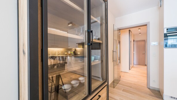 A modern kitchen with a glass cabinet, wooden flooring, and a built-in oven. - Moorea City Center Apartment (Middelkerke)