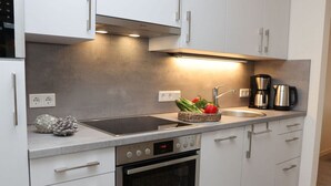 A modern kitchen with white cabinets, a stainless steel range hood, a double sink, and a built-in oven. - My Baltic Sea Place House by the sea 7 (Niesgrau)