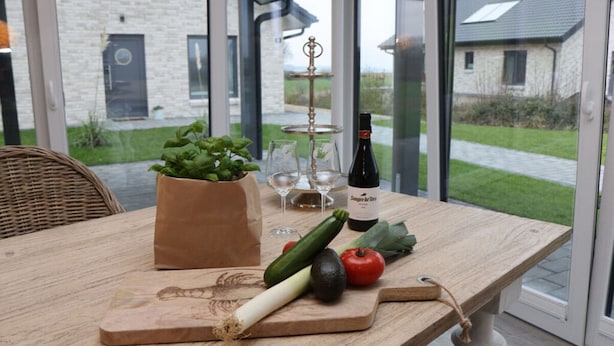 A wooden table with a cutting board, a bottle of wine, a glass, a potted plant, and fresh vegetables. - My Baltic Sea Place House by the sea 7 (Niesgrau)