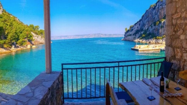 A stone balcony with a wooden table and chairs overlooking a turquoise sea and rocky coastline. - Apartments Vela Stiniva - Two Bedroom Apartment With Sea View and Terrace (Jelsa)