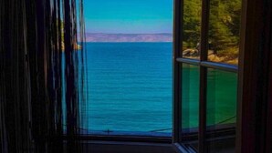 A room with a large window offering a view of the sea and a forested area. - Apartments Vela Stiniva - Two Bedroom Apartment With Sea View and Terrace (Jelsa)