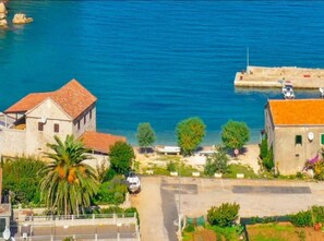 A coastal building with a red-tiled roof, a parking area, and a view of the sea. - Apartments Vela Stiniva - Two Bedroom Apartment With Sea View and Terrace (Jelsa)