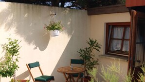A small patio area with two wooden chairs and a table, surrounded by potted plants and a hanging flower pot. - Little Beach Flea Comfortable Holiday Residence (Wangerooge)