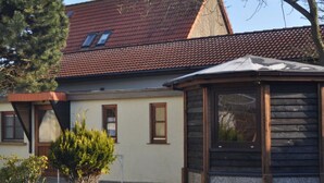 A house with a red-tiled roof, a wooden conservatory, and a small tree in the yard. - Little Beach Flea Comfortable Holiday Residence (Wangerooge)