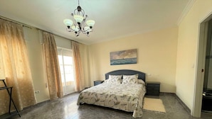 A bedroom with a bed, a nightstand, a dresser, a chandelier, and a painting on the wall. - Belvilla by OYO Holiday Home in Los Alcazares (Los Alcazares)