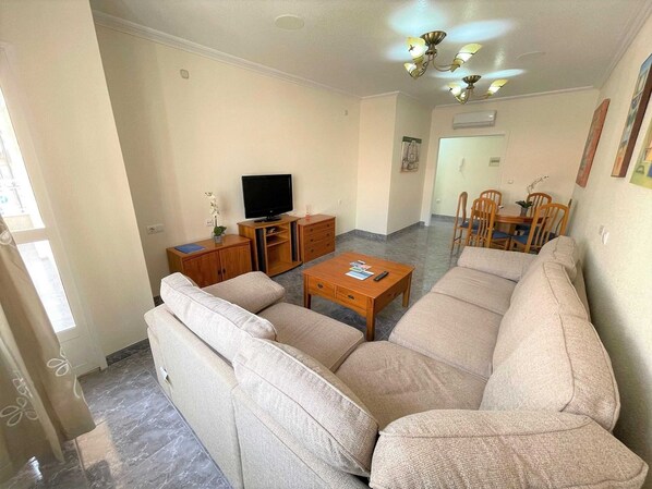 A living room with a sofa, TV, wooden side table, and a dining area with chairs. - Belvilla by OYO Holiday Home in Los Alcazares (Los Alcazares)