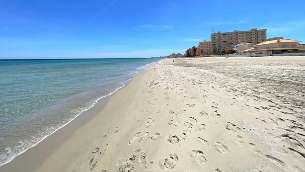 A sandy beach with footprints, a clear blue sky, and buildings in the background. - Belvilla by OYO Holiday Home in Los Alcazares (Los Alcazares)