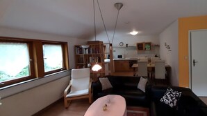 Un salon comprenant un canapé, un fauteuil, une petite table et une bibliothèque. Il y a également un coin cuisine avec un four à micro-ondes et des placards.