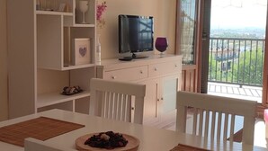 Un salon moderne avec une télévision, une table à manger où se trouve une assiette de nourriture, et un balcon avec vue.