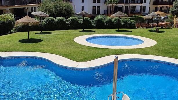 Une piscine dotée d’un toboggan intégré, entourée d’une pelouse bien entretenue et de parasols.