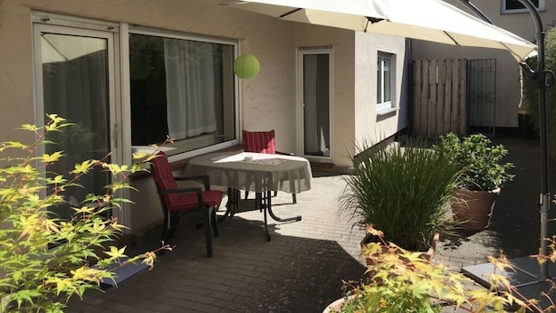 Une terrasse avec une table et des chaises, un grand parasol et des plantes en pot.