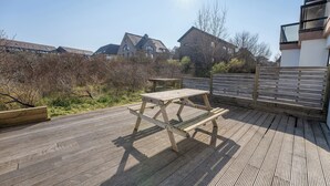 Een houten terras met een picknicktafel, omgeven door een houten omheining en uitzicht op woongebouwen.