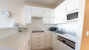 Een kleine keuken met witte kastjes, een magnetron, een broodrooster en een spoelbak.