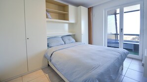 Ein Schlafzimmer mit Bett, Einbauschränken und einer Glasschiebetür zu einem Balkon.