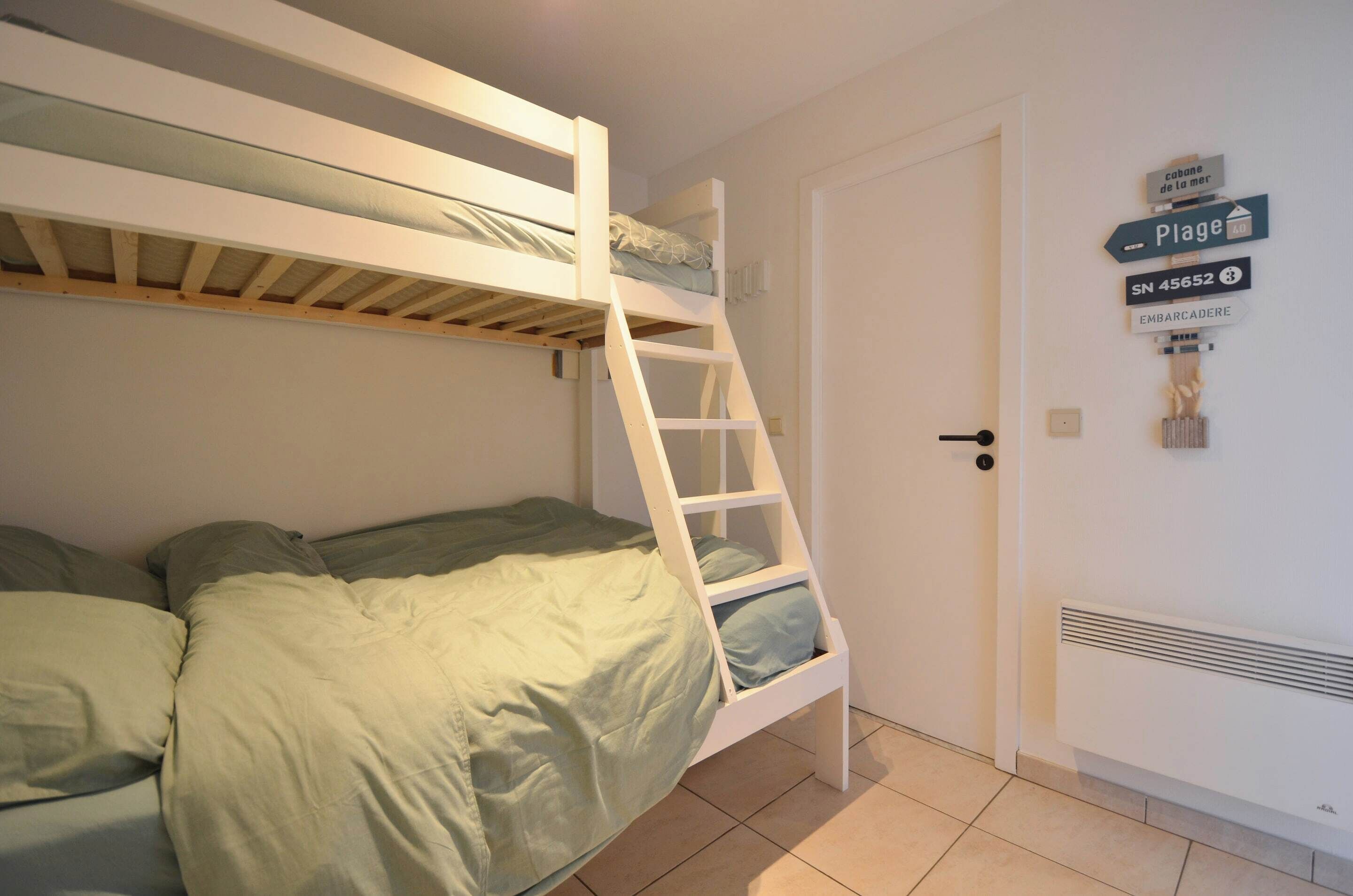 Ein Stockbett mit einer Leiter, eine Tür mit einem Schild und eine Heizung.
