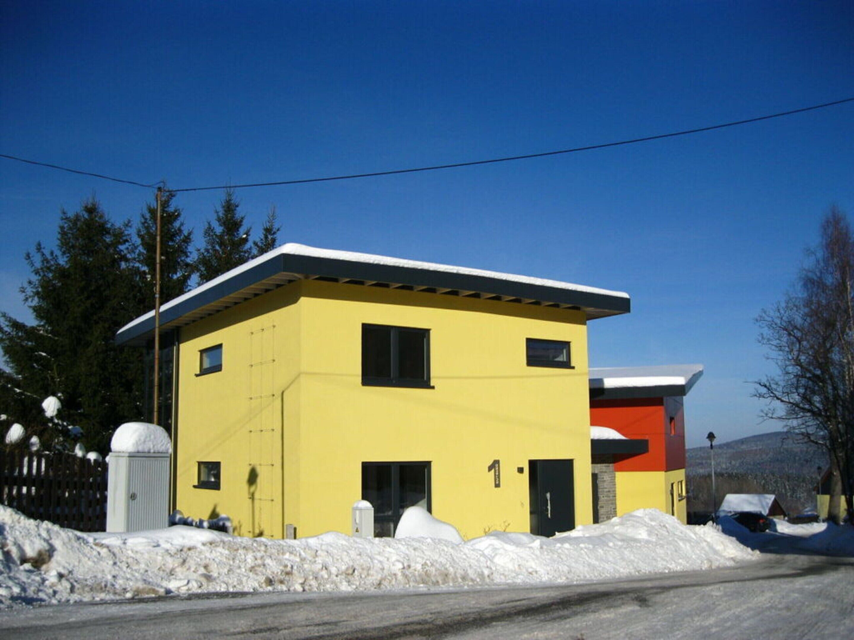 A yellow two-story building with a flat roof, a small porch, and a door.
