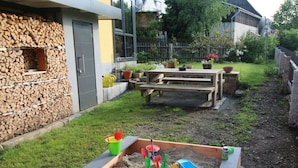 Un arenero con juguetes y un banco de madera en un patio trasero.