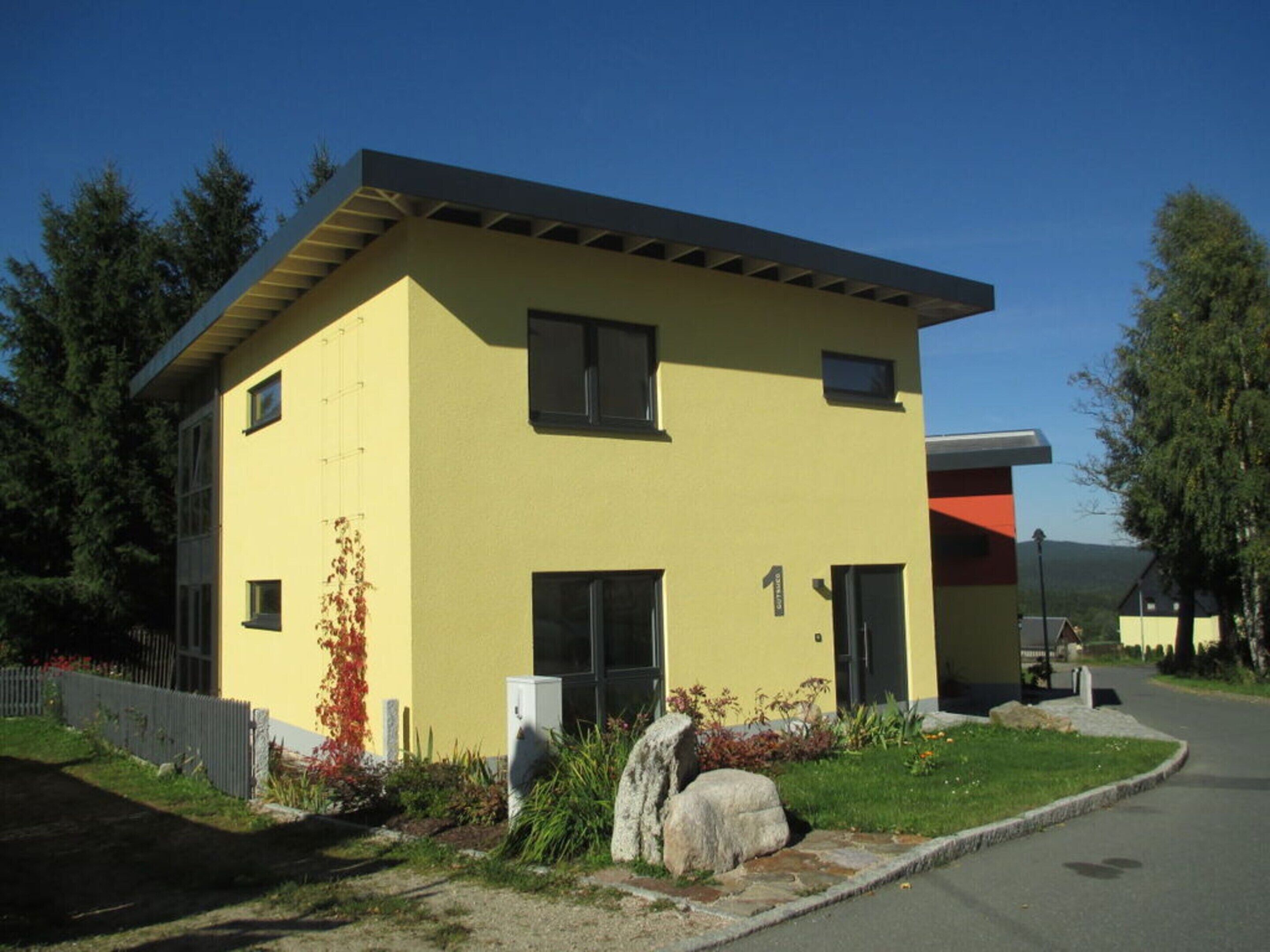 A modern two-story building with a yellow facade, large windows, and a visible entrance.