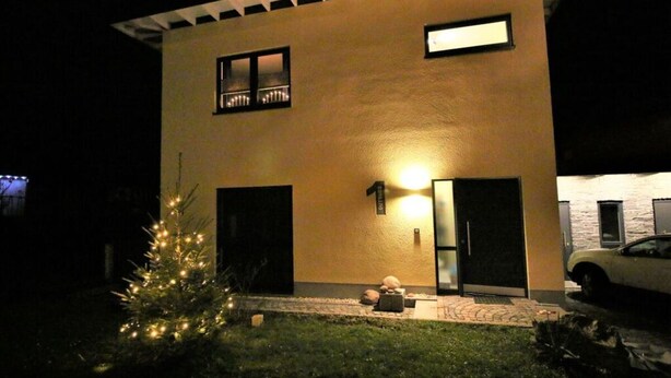 Una casa moderna de dos pisos con una entrada bien iluminada y un pequeño árbol de Navidad en el jardín delantero.