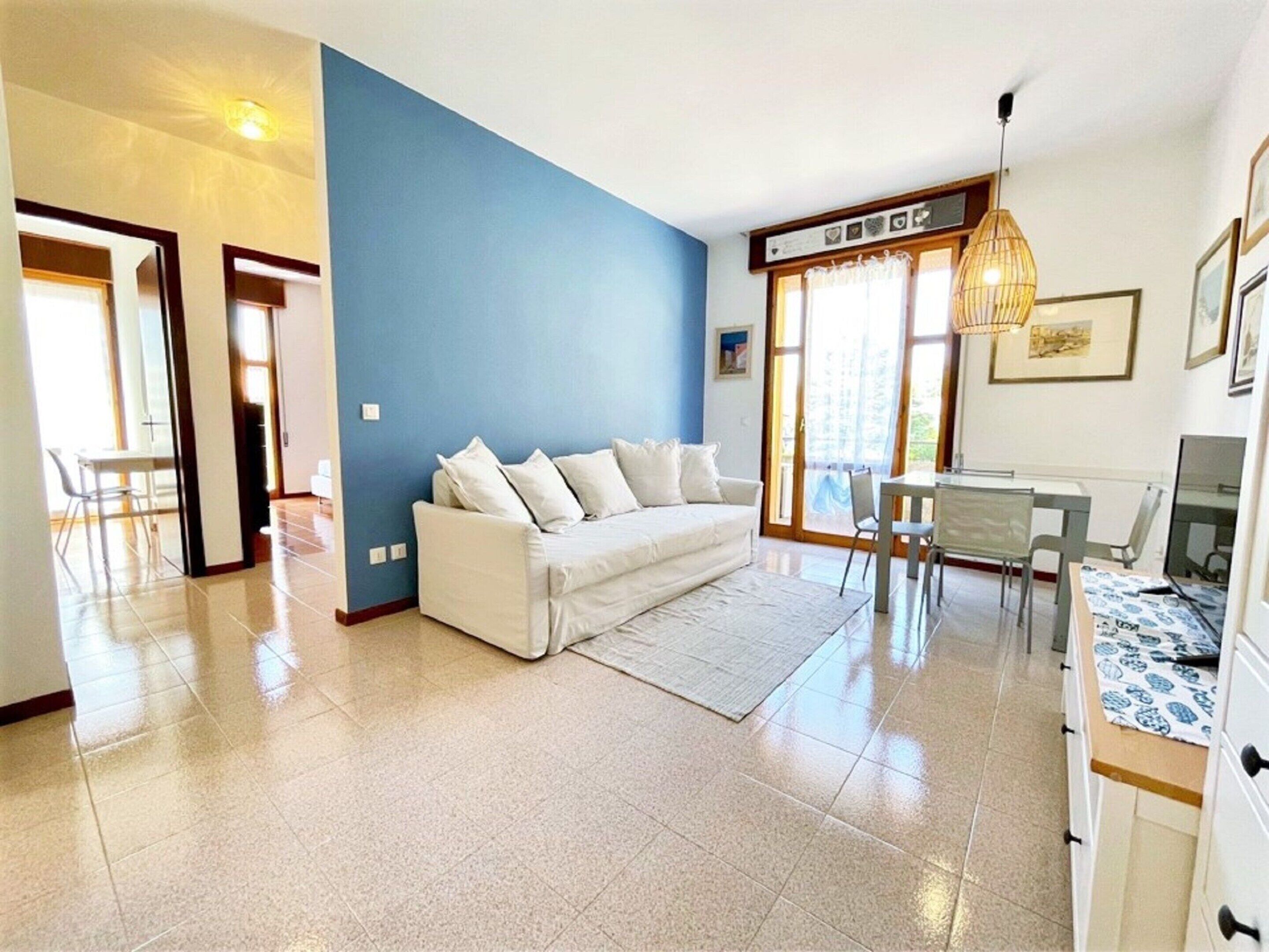 Una sala de estar moderna con un sofá blanco, una mesa de comedor de vidrio y una pared de acento azul.