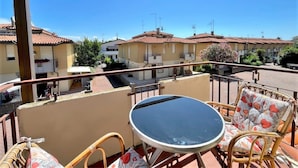 A balcony with a table and wicker chairs, overlooking a residential street with terracotta-roofed houses. - Apartment Near Porto Santa Margherita Beach (Caorle)