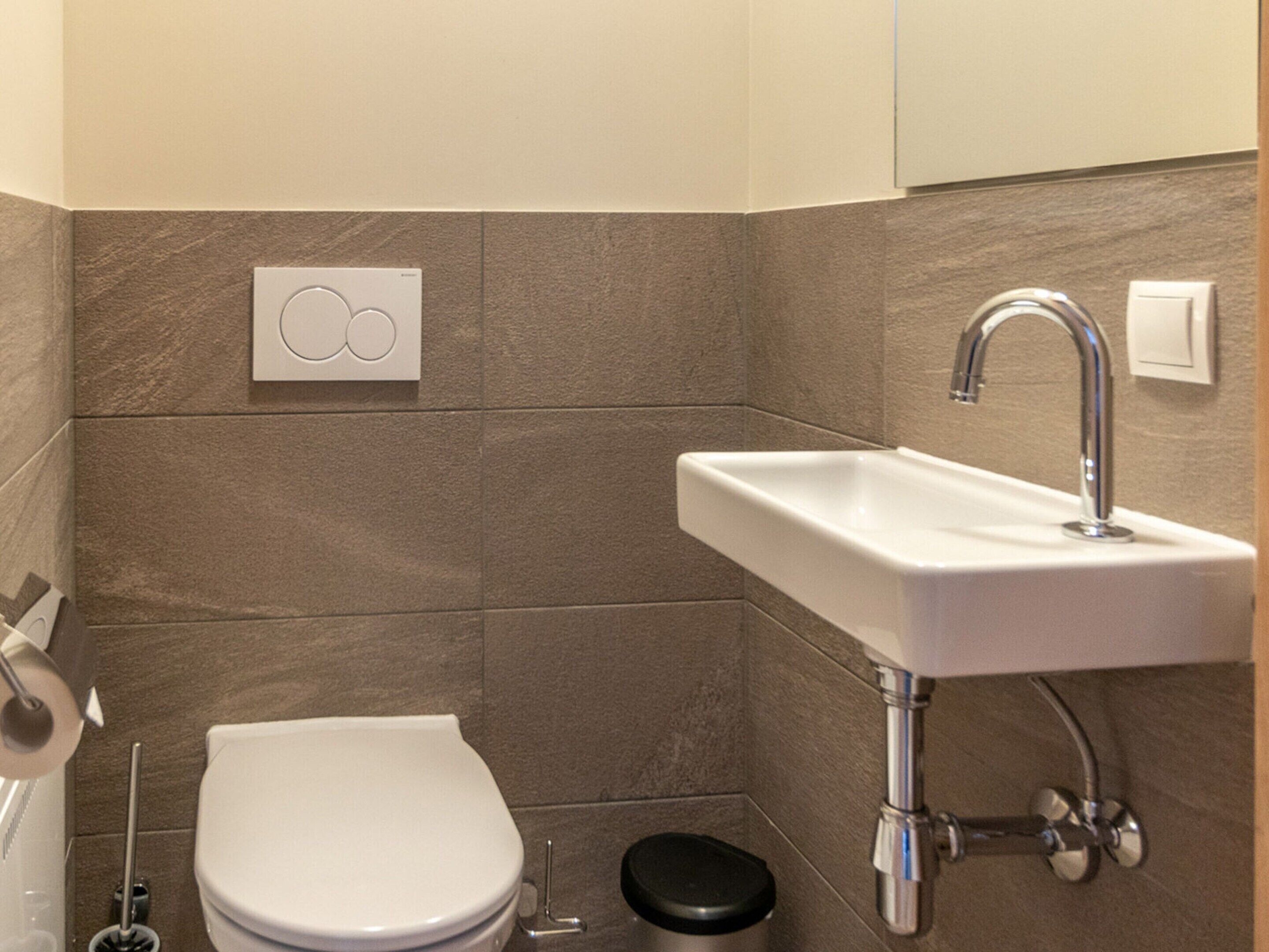 Une salle de bain moderne avec des toilettes blanches, un lavabo doté d’un robinet chromé et une poubelle.