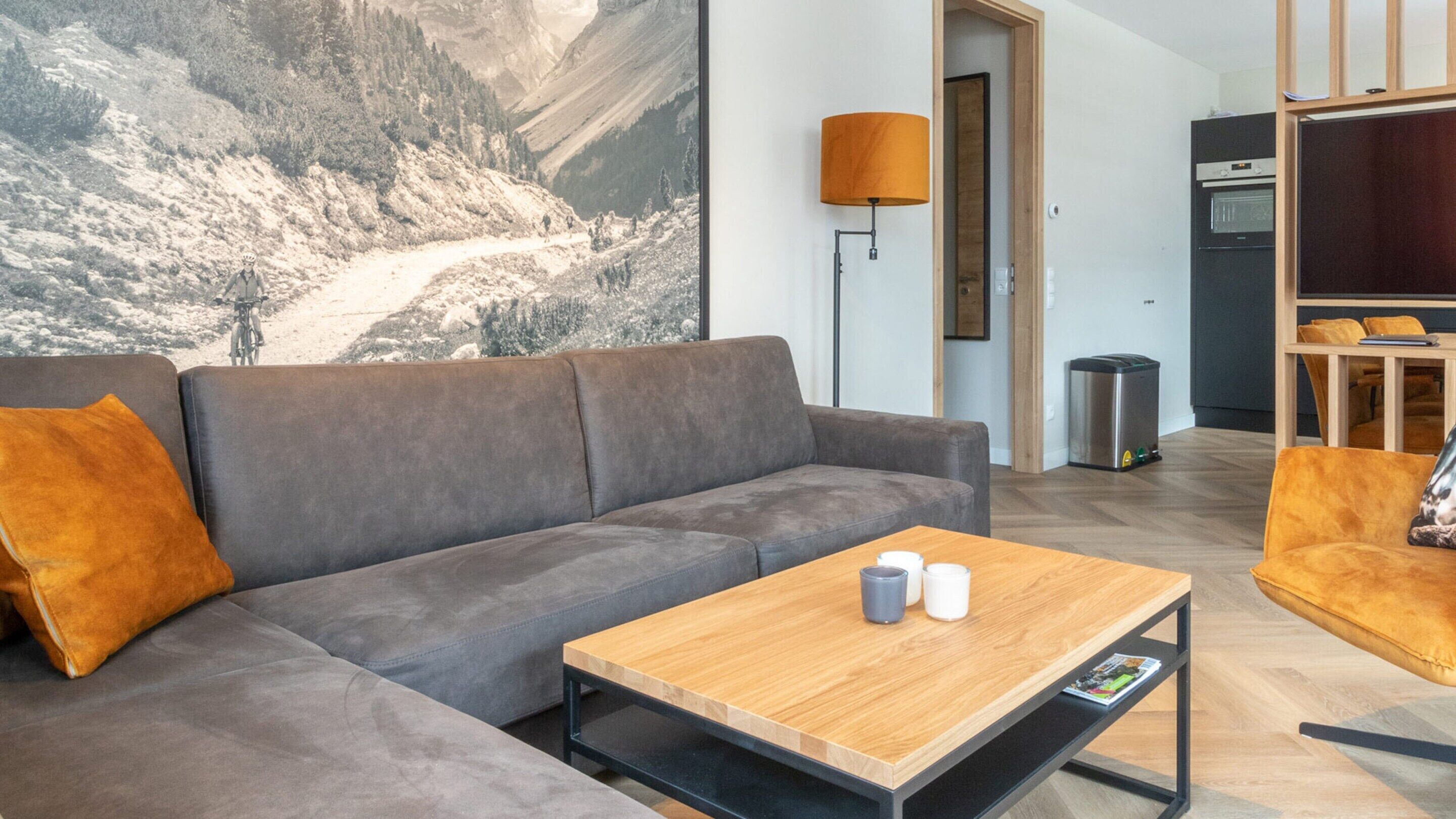 Un salon moderne avec un canapé gris, une table basse en bois et un tableau représentant un paysage de montagne.