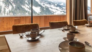 Ein Essbereich mit einem Tisch für vier Personen, Stühlen und Blick auf verschneite Berge durch große Fenster.