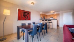 A modern living room with a dining table, chairs, a red sofa, a lamp, and a kitchen in the background. - Apartment in Koksijde Near the Sea (Koksijde)